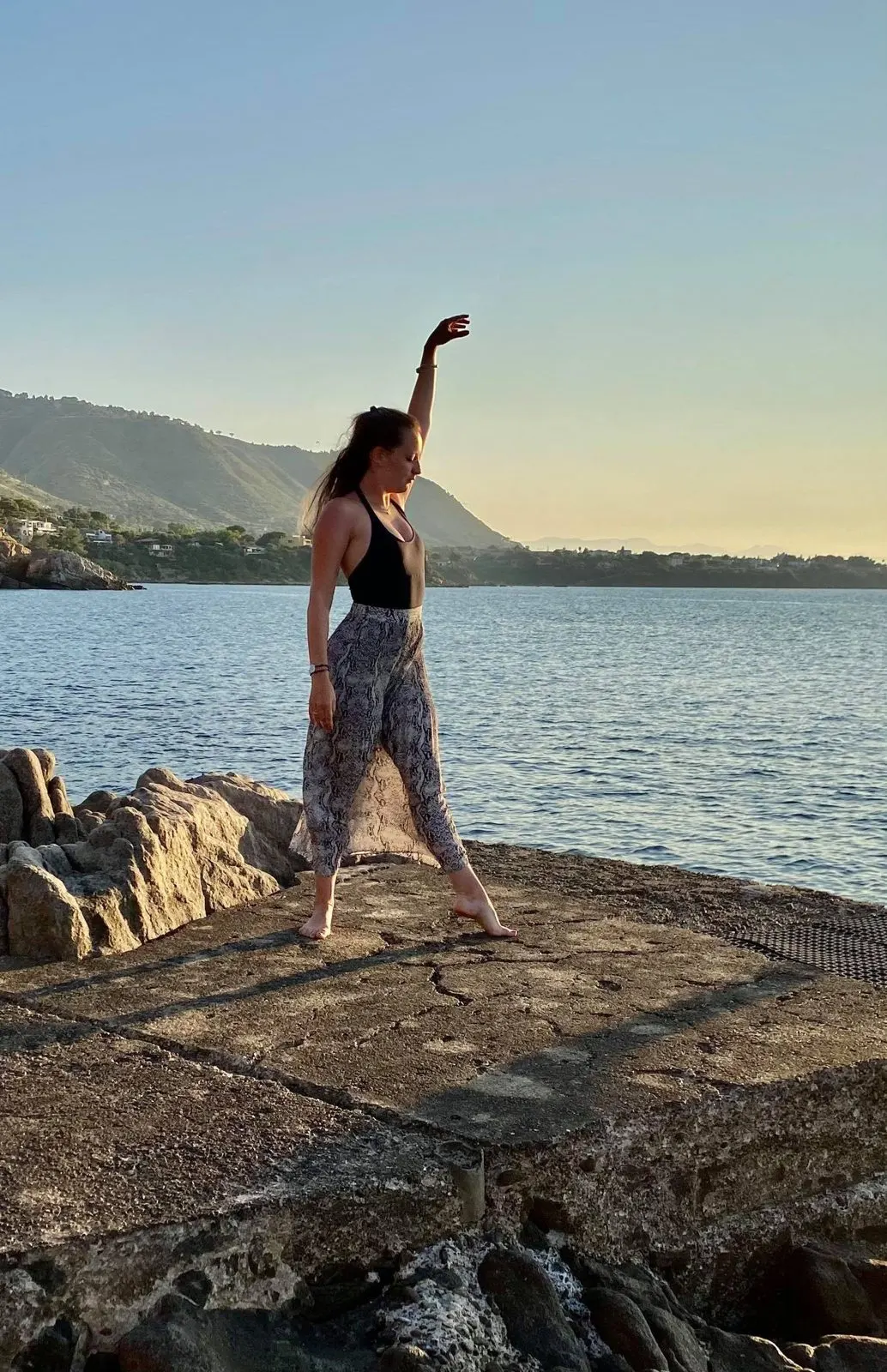 Pauline en équilibre sur un rocher face à la mer, un bras levé